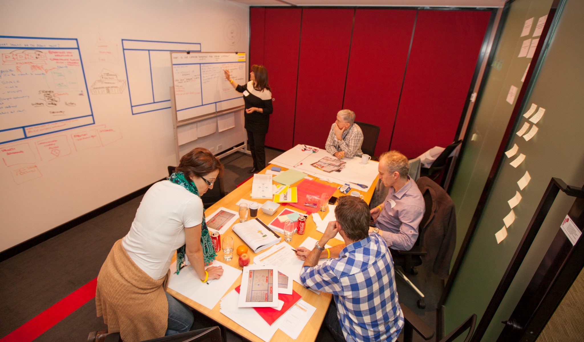 Participants collaborating around a table and storyboard wall during a Fundamental Academy working session.
